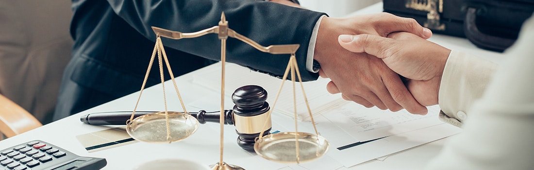 two people shaking hands with a gavel and scales in the foreground